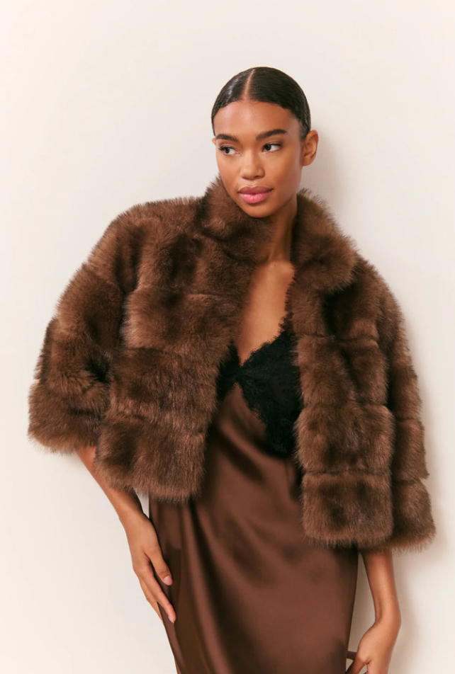 Woman wearing a brown fur coat over a brown dress against a white background