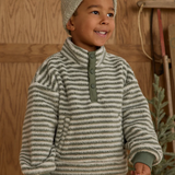 Child wearing a striped sweater and hat in a wooden interior setting