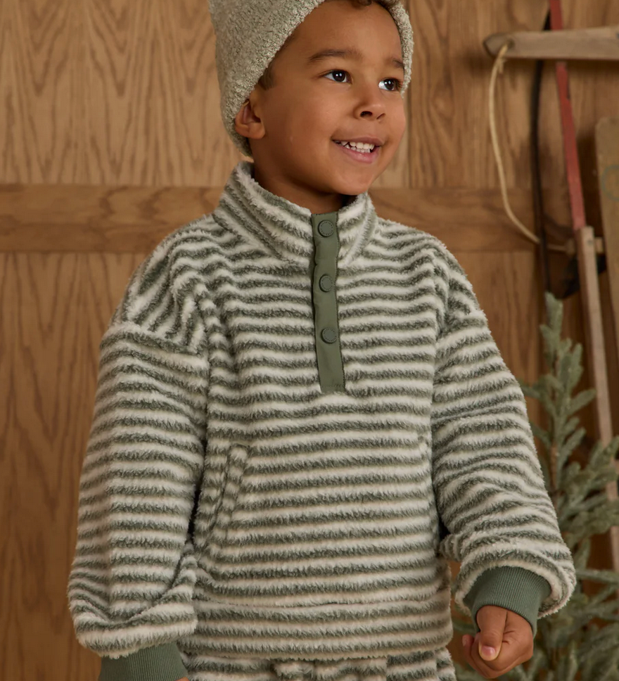 Child wearing a striped sweater and hat in a wooden interior setting
