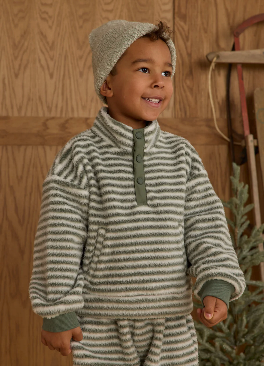 Child wearing a striped sweater and hat in a wooden interior setting